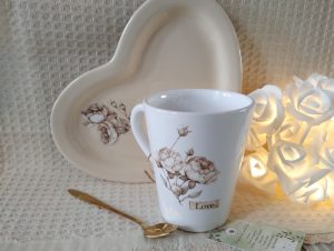 Taza de té, con cucharita de diseño y plato de cerámica, en forma de corazón.