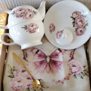 Box con set de té, con tazon, tetera, plato redondo, de cerámica con estampado de flores. Incluye cucharita de diseño, dorada, y mantel individual de lienzo de algodon, estampado con flores y mariposas