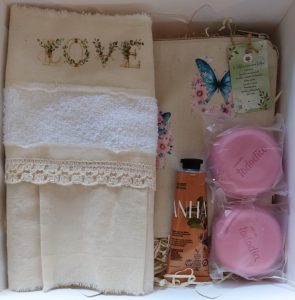 Box spa, con neceser de tela, estampado con mariposas. Toalla de mano, con volado, puntilla, y estampa. Jabones y crema de mano, marca Natura.