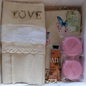 Box spa, con neceser de tela, estampado con mariposas. Toalla de mano, con volado, puntilla, y estampa. Jabones y crema de mano, marca Natura.